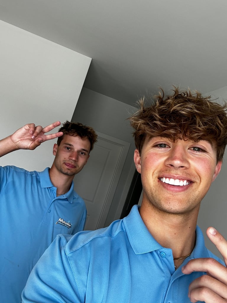 Two young men in blue polo shirts smiling and gesturing at the camera indoors