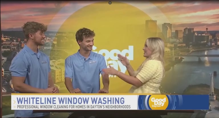 Two men in blue shirts speak with a woman in yellow on a TV show set featuring Dayton skyline backdrop and Whiteline Window Washing segment banner